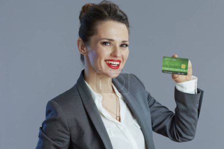 Foto de Feliz elegante dueño de la pequeña empresa mujer en traje gris con tarjeta de crédito sobre fondo gris. - Imagen libre de derechos