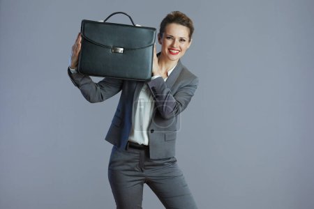Foto de Feliz mujer de mediana edad trabajadora en traje gris con maletín aislado sobre fondo gris. - Imagen libre de derechos