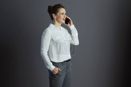 Foto de Feliz elegante dueño de una pequeña empresa mujer en blusa blanca hablando en un teléfono móvil y mirando a la distancia aislada en gris. - Imagen libre de derechos