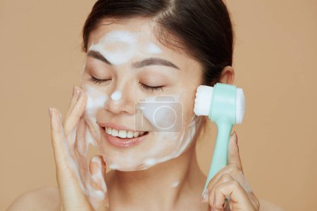 Photo for Young woman with massager washing face isolated on beige background. - Royalty Free Image