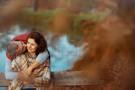 Foto de Hola otoño. sonriente pareja romántica en el parque besándose mientras está sentado en el banco. - Imagen libre de derechos