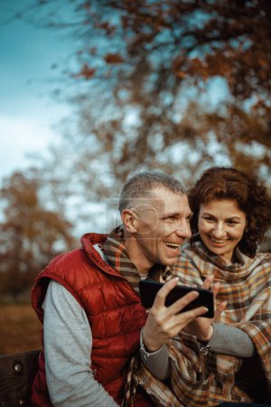 Foto de Hola otoño. familia romántica sonriente en el parque usando teléfono inteligente. - Imagen libre de derechos