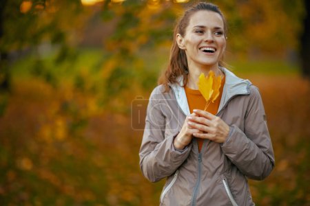 Foto de Hola otoño. sonriente mujer en forma en ropa de fitness en el parque con hoja de otoño. - Imagen libre de derechos