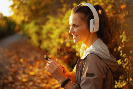 Photo for Hello autumn. smiling trendy woman in fitness clothes in the park with headphones. - Royalty Free Image