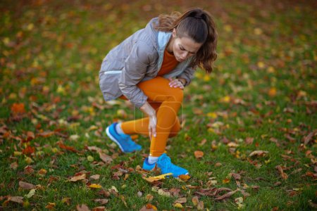 Foto de Hola otoño. mujer en forma triste en ropa de fitness en el parque con dolor en las piernas. - Imagen libre de derechos