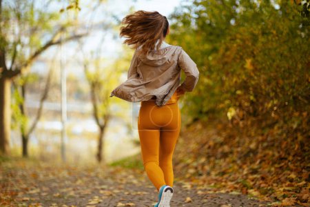 Foto de Hola otoño. Visto desde atrás mujer en ropa de fitness en el parque corriendo. - Imagen libre de derechos