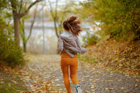 Photo for Hello autumn. Seen from behind middle aged woman in fitness clothes in the park running. - Royalty Free Image