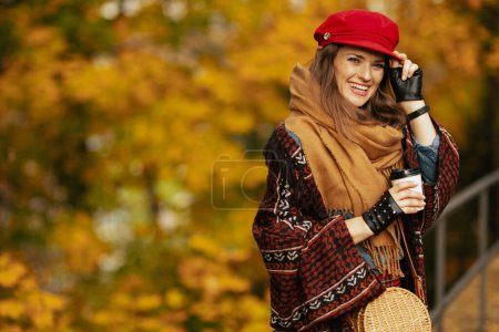 Téléchargez les photos : Bonjour l'automne. Portrait de heureuse femme d'âge moyen en chapeau rouge avec écharpe, gants, sac et café dans le parc de la ville. - en image libre de droit