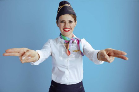 Photo for Happy stylish stewardess woman on blue background in uniform showing where the exits are. - Royalty Free Image