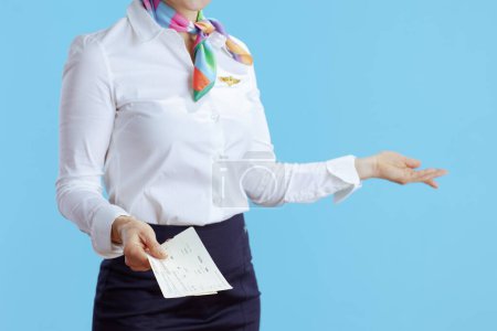 Téléchargez les photos : Gros plan sur la femme hôtesse élégante sur fond bleu en uniforme avec des billets d'avion accueillant. - en image libre de droit