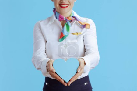 Téléchargez les photos : Gros plan sur femme hôtesse de l'air moderne isolée sur fond bleu en uniforme montrant coeur. - en image libre de droit