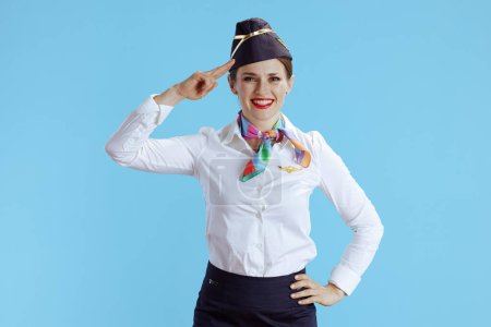 Photo for Smiling elegant female flight attendant isolated on blue background in uniform salutes. - Royalty Free Image