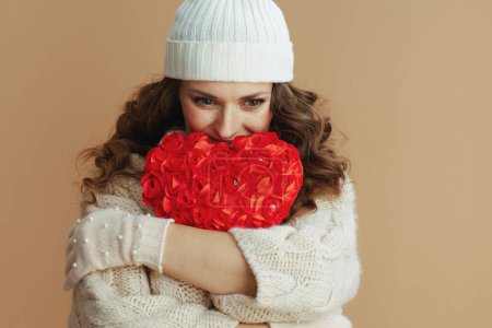 Photo for Hello winter. pensive trendy woman in beige sweater, mittens and hat on beige background with red heart. - Royalty Free Image