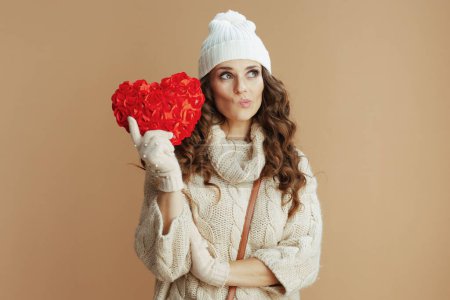 Téléchargez les photos : Bonjour l'hiver. coûteuse élégante femme en pull beige, mitaines et chapeau avec coeur rouge isolé sur beige. - en image libre de droit