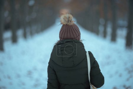 Photo for Seen from behind woman in green coat and brown hat outdoors in the city park in winter with beanie hat. - Royalty Free Image