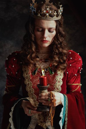 Photo for Medieval queen in red dress with candle and crown on dark gray background. - Royalty Free Image