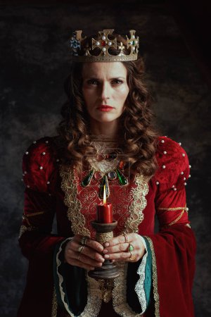 Foto de Reina medieval en vestido rojo con vela y corona sobre fondo gris oscuro. - Imagen libre de derechos