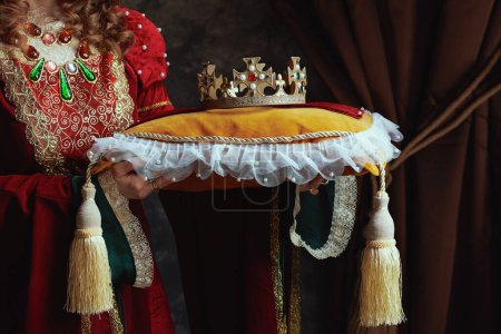 Photo for Closeup on medieval queen in red dress with crown on pillow on dark gray background. - Royalty Free Image