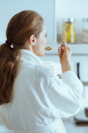 Photo for Young woman in bathrobe eating breakfast. rear view - Royalty Free Image