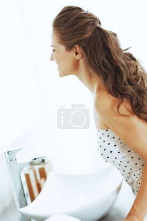 Téléchargez les photos : Heureuse jeune femme regardant dans le miroir dans la salle de bain - en image libre de droit