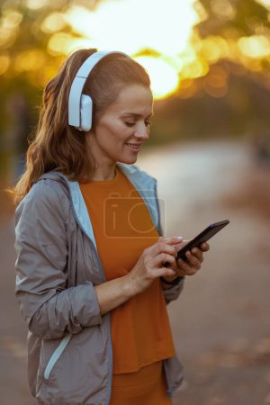 Téléchargez les photos : Bonjour l'automne. femme d'âge moyen en vêtements de fitness dans le parc avec écouteurs. - en image libre de droit