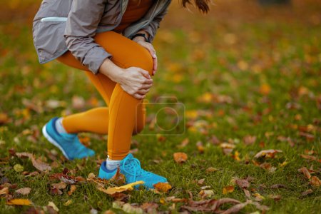 Foto de Hola otoño. Primer plano de la mujer en ropa de fitness en el parque tiene una lesión en la pierna. - Imagen libre de derechos