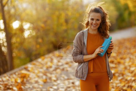 Téléchargez les photos : Bonjour l'automne. forme souriante 40 ans femme en vêtements de fitness dans le parc avec bouteille d'eau. - en image libre de droit