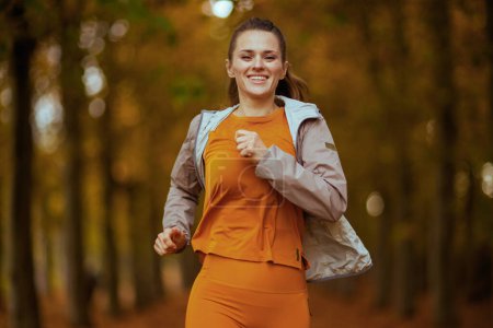 Foto de Hola otoño. sonriente mujer de moda de 40 años en ropa de fitness en el parque corriendo. - Imagen libre de derechos