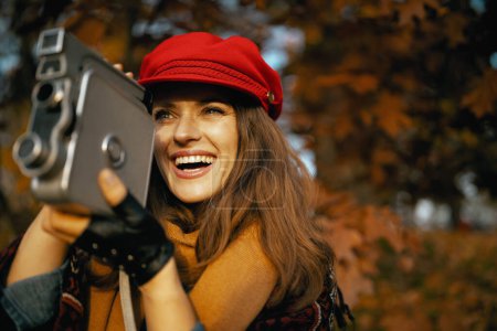 Photo for Hello autumn. happy stylish 40 years old woman in red hat with retro video camera, scarf and gloves in the city park. - Royalty Free Image