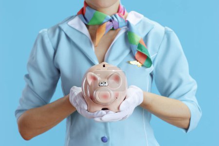 Photo for Closeup on stewardess woman against blue background in blue uniform with piggy bank. - Royalty Free Image