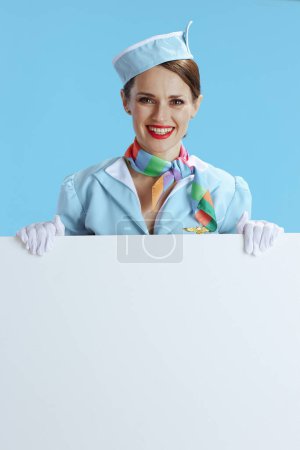 Téléchargez les photos : Heureuse élégante hôtesse de l'air femme sur fond bleu uniforme bleu montrant tableau blanc. - en image libre de droit