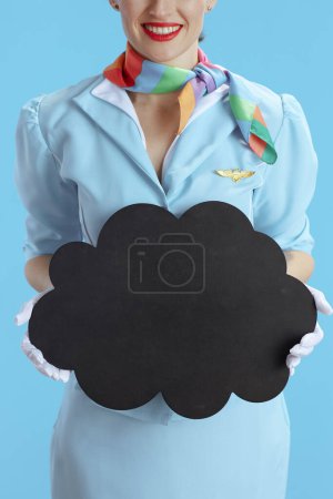 Photo for Closeup on flight attendant woman against blue background in blue uniform showing blank cloud shape board. - Royalty Free Image