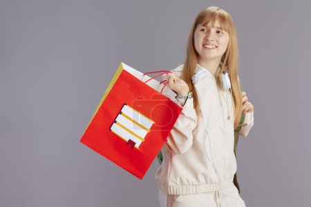 Photo for Happy trendy girl in beige tracksuit with shopping bag and headphones isolated on grey. - Royalty Free Image