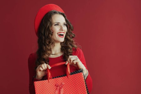 Foto de Feliz San Valentín. sonriente mujer elegante en vestido rojo y boina contra fondo rojo con bolsas de compras. - Imagen libre de derechos