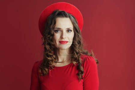 Téléchargez les photos : Joyeux Valentin. Portrait de femme moderne de 40 ans avec de longs cheveux ondulés en robe rouge et béret sur fond rouge. - en image libre de droit