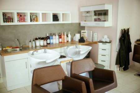 Téléchargez les photos : Salon de beauté moderne avec chaises, bouteilles de produits de soins capillaires et unité de lavage de salon. - en image libre de droit