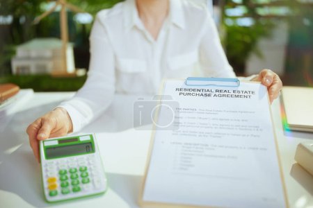 Photo for Eco real estate business. Closeup on business woman in green office in white blouse with calculator, clipboard and document. - Royalty Free Image