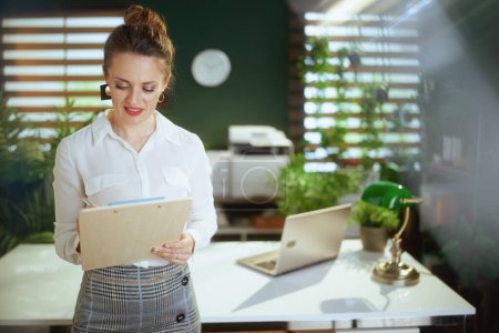 Photo for Sustainable real estate business. pensive young woman real estate agent in modern green office in white blouse with clipboard. - Royalty Free Image