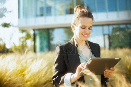 Foto de Feliz mujer moderna de mediana edad trabajadora en el distrito de negocios en chaqueta negra usando tableta PC. - Imagen libre de derechos