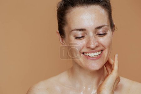 Téléchargez les photos : Heureux moderne femelle avec humide visage lavage sur fond beige. - en image libre de droit