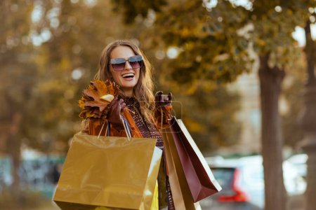 Téléchargez les photos : Bonjour octobre. heureuse femme élégante en trench-coat orange avec des sacs à provisions et des feuilles jaune automne dans la ville. - en image libre de droit