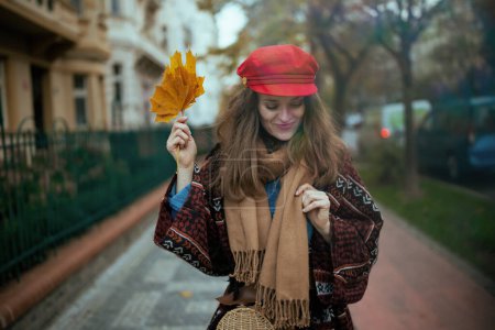 Foto de Hola otoño. mujer elegante feliz en sombrero rojo con hojas de otoño, bufanda y bolso en la ciudad. - Imagen libre de derechos
