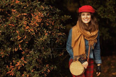 Foto de Hola otoño. feliz mujer de moda de 40 años con camisa vaquera y sombrero rojo con bufanda, guantes y bolso en el parque de la ciudad. - Imagen libre de derechos