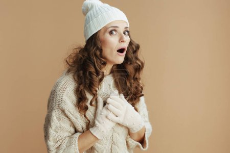 Téléchargez les photos : Bonjour l'hiver. femme tendance surprise en pull beige, mitaines et chapeau sur fond beige. - en image libre de droit