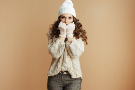 Téléchargez les photos : Bonjour l'hiver. triste femme à la mode en pull beige, mitaines et chapeau sur fond beige mains chauffantes. - en image libre de droit