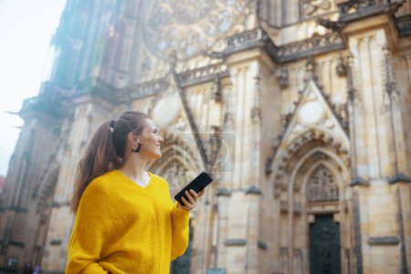 Téléchargez les photos : Femme élégante et souriante en chemisier jaune à Prague République tchèque avec smartphone ayant la visite à pied et la marche. - en image libre de droit