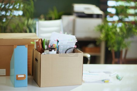 Téléchargez les photos : Un nouveau boulot. table dans un bureau vert moderne avec effets personnels dans une boîte en carton. - en image libre de droit
