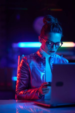 Photo for Neon metaverse futuristic concept. modern woman in glasses with laptop using smartphone in modern office. - Royalty Free Image