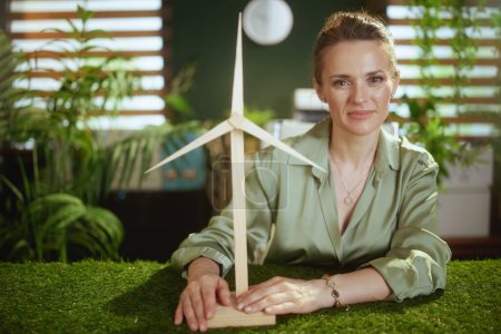 Photo for Time to go eco. elegant middle aged small business owner woman in green blouse in modern green office with windmill - Royalty Free Image