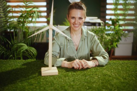 Foto de Hora de hacer eco. sonriente elegante mediana edad dueño de la pequeña empresa mujer en blusa verde en moderna oficina verde con molino de viento - Imagen libre de derechos